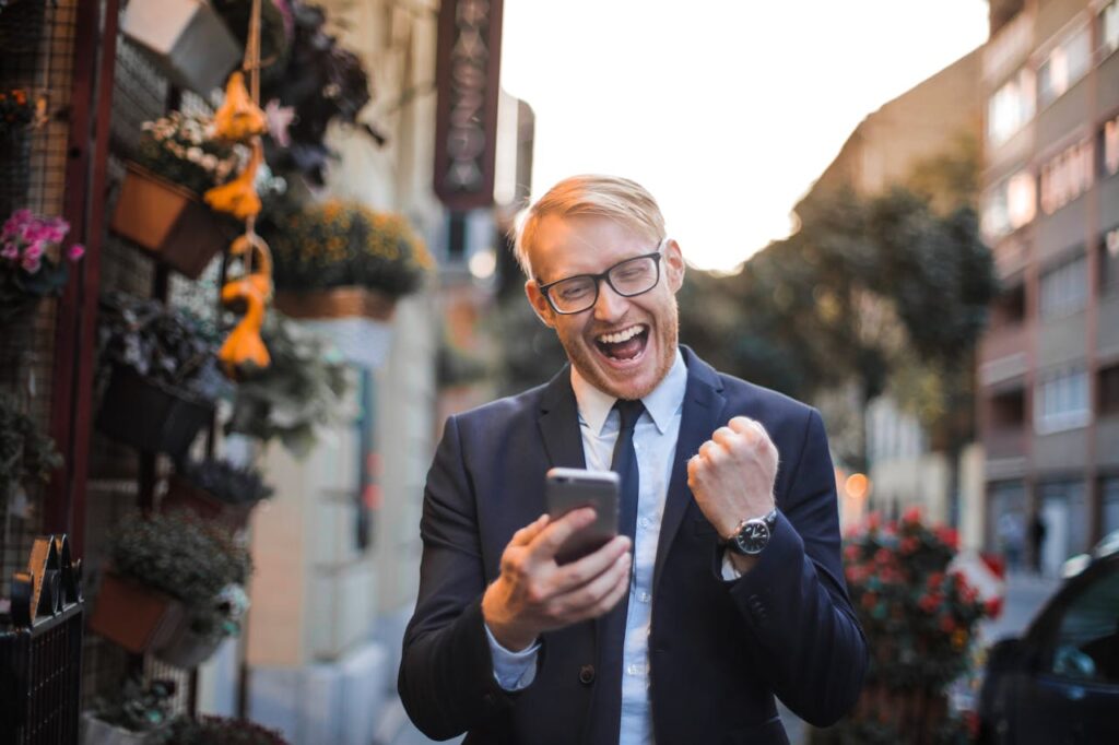 pexels-photo-3760260 A joyful man in a suit celebrates good news on his smartphone in an urban street setting.